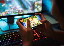 A teenage boy plays a mobile game in front of a gaming PC